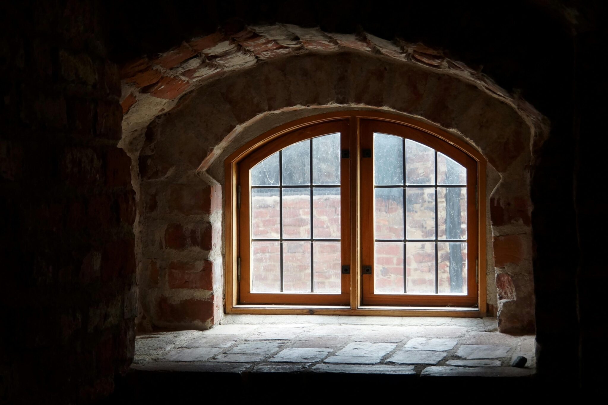 Atmospheric interior view of a brick arch window with wooden frame under soft light.