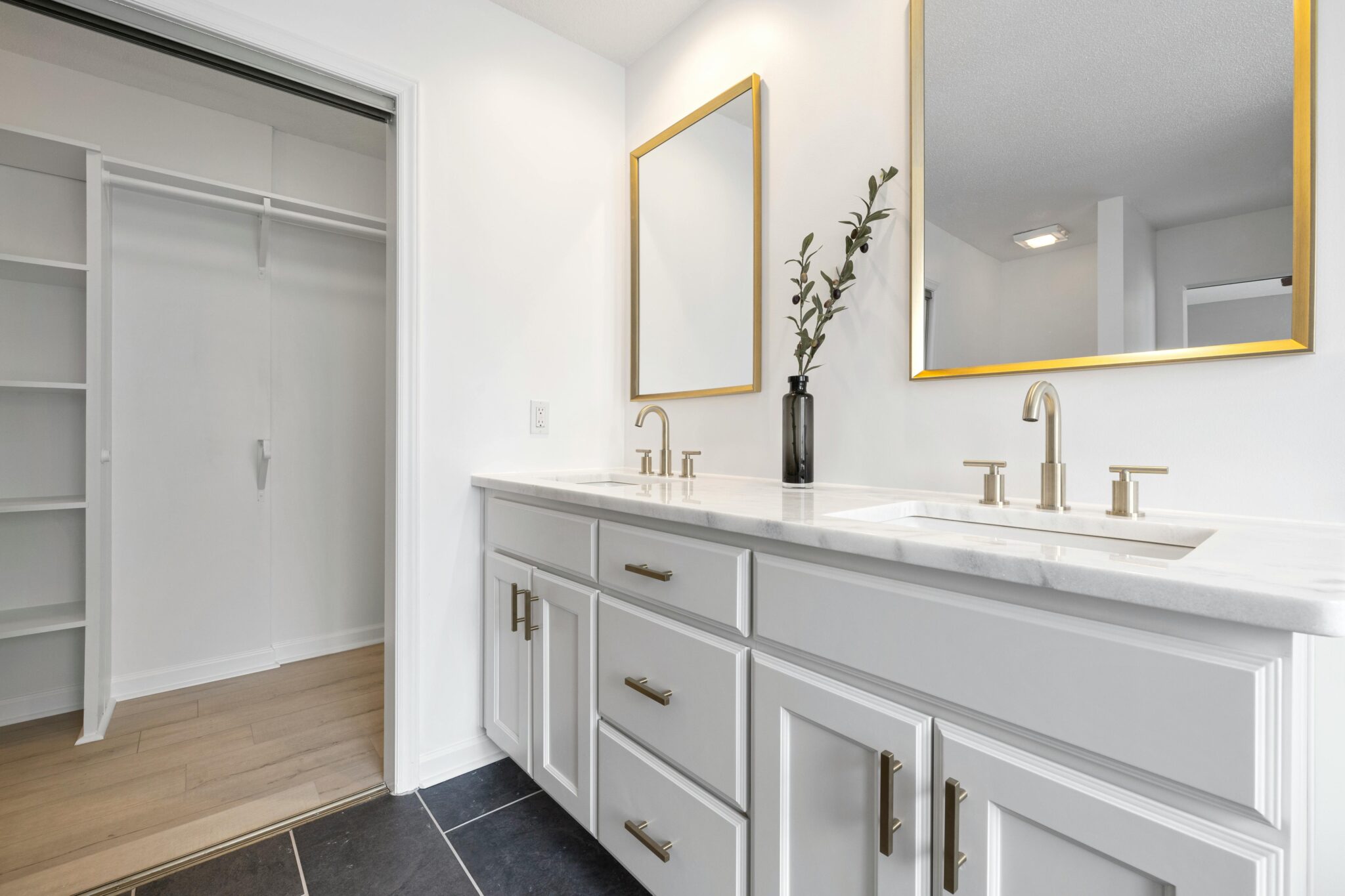 Bright minimalist bathroom with dual sinks, marble countertops, and gold-framed mirrors.