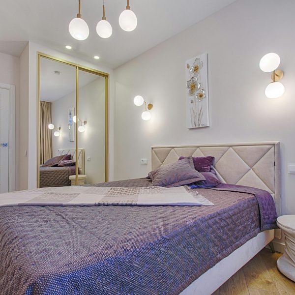 Elegant bedroom with purple decor, modern lighting, and mirror wardrobe.