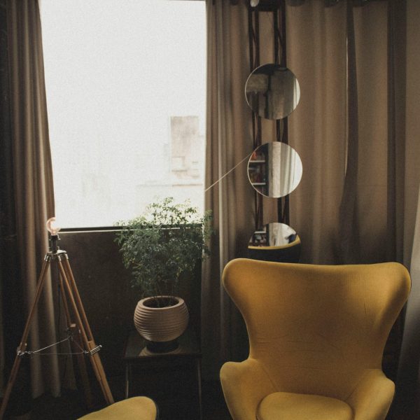 Warm and stylish room featuring yellow chair, plants, and mirrors.