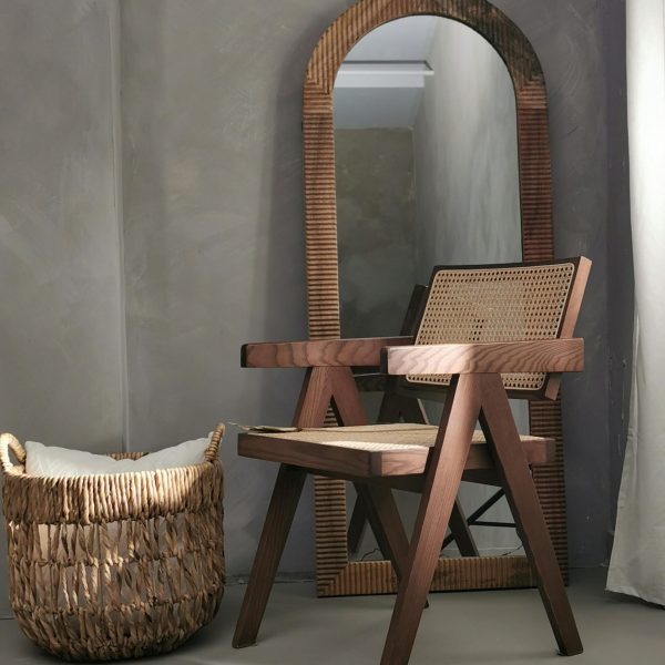 Cozy bohemian corner with a wooden armchair, round mirror, and rattan basket.