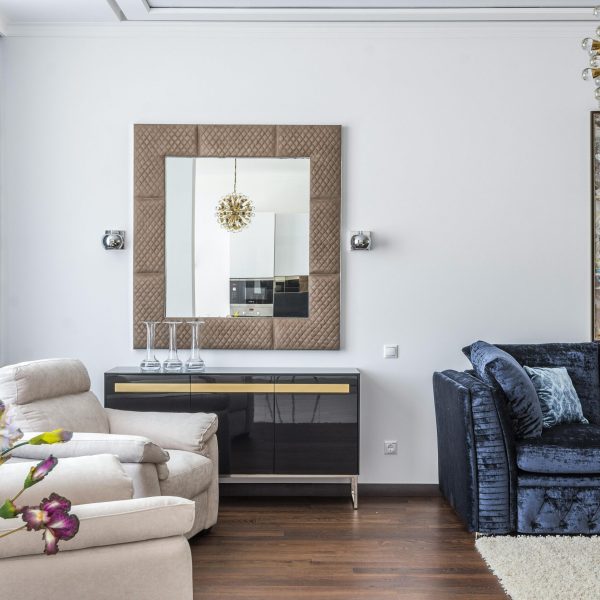 Stylish living room with armchair, velvet sofa, mirror, and floral decorations.