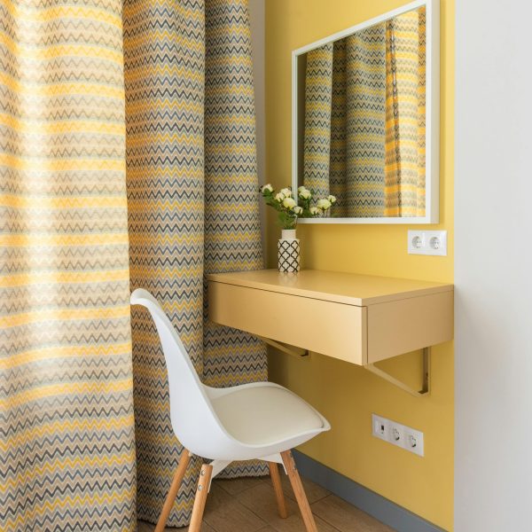 Elegant corner vanity setup with mirror, yellow zigzag curtains, and modern chair.
