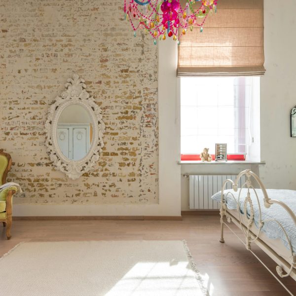 Elegant vintage bedroom featuring a brick wall, ornate mirror, and colorful chandelier.