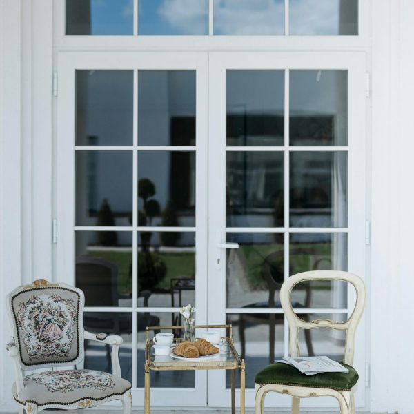 A serene patio scene featuring vintage chairs and a cart with breakfast items like croissants and coffee.
